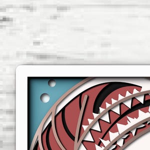 May include: A layered paper art piece featuring a stylized red and white shark mouth with sharp teeth. The design includes a blue background with two circular cutouts, creating a dimensional effect with stacked paper layers in red, white, and blue.