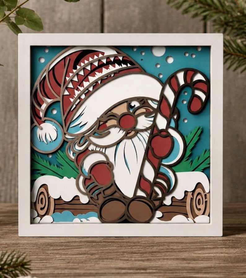 May include: A square white-framed layered paper art piece featuring a gnome wearing a red and white hat, holding a red and white striped candy cane. The gnome has a white beard and sits on a brown log against a teal background with white dots.