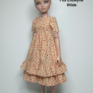 K&ouml;nnte beinhalten: Eine Puppe in einem cremefarbenen Kleid mit rotem Blumenmuster. Das Kleid hat kurze &Auml;rmel und einen Stufenrock. Der Text "Fits Ellowyne Wilde" ist sichtbar.
