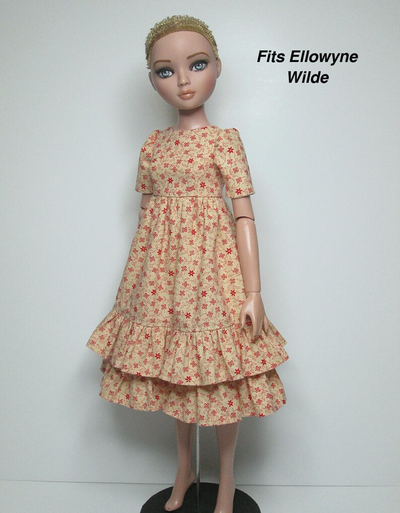 K&ouml;nnte beinhalten: Eine Puppe in einem cremefarbenen Kleid mit rotem Blumenmuster. Das Kleid hat kurze &Auml;rmel und einen Stufenrock. Der Text "Fits Ellowyne Wilde" ist sichtbar.