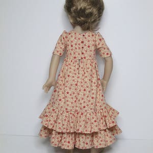 K&ouml;nnte beinhalten: Puppe in einem cremefarbenen Kleid mit rotem Blumenmuster. Das Kleid hat kurze &Auml;rmel, ein figurbetontes Oberteil und einen gestuften, ger&uuml;schten Rock. Die Puppe hat kurze, hellbraune Haare.