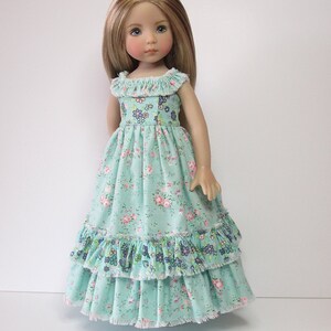K&ouml;nnte beinhalten: Eine Puppe tr&auml;gt ein hellblaues Kleid mit Blumenmuster und mehreren R&uuml;schen. Das Kleid hat einen wei&szlig;en Spitzenbesatz.
