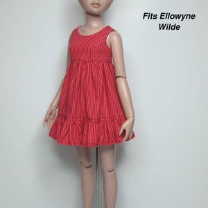 K&ouml;nnte beinhalten: Ein rotes gestreiftes Puppenkleid mit R&uuml;schensaum. Das &auml;rmellose Kleid wird an einer Puppe mit blonden Haaren und blauen Augen gezeigt. Der Text "Fits Ellowyne Wilde" ist auf der rechten Seite des Bildes zu sehen.