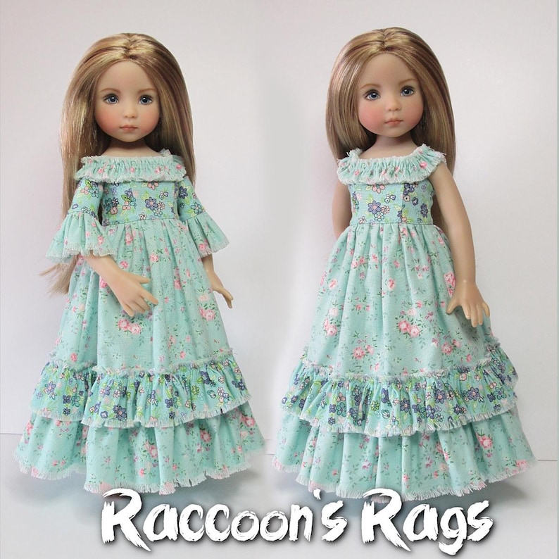 K&ouml;nnte beinhalten: Zwei Puppen tragen ein hellblaues Kleid mit Blumenmuster und mehreren R&uuml;schenlagen. Das Kleid hat einen wei&szlig;en Spitzenbesatz. Die Puppen haben langes blondes Haar. Das Bild enth&auml;lt den Text "Raccoon's Rags".