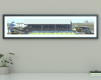 May include: A framed panoramic print of a soccer stadium with a large crowd of fans in the stands. The stadium is a classic design with a white roof and blue seats. The print is in a black frame.