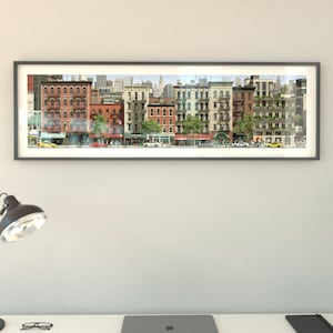 May include: A framed panoramic print of a city street scene. The artwork shows a row of buildings with different architectural styles, including brick and stone facades. Cars and pedestrians are visible on the street. The sky is a light blue with a cityscape in the background.