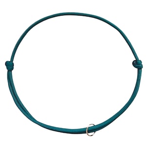 Puede incluir: Una pulsera de cordón color verde azulado oscuro con una estructura de nailon lisa y redondeada. La pulsera se asegura con dos nudos deslizantes ajustables a cada lado e incluye un pequeño anillo metálico plateado en el cordón.