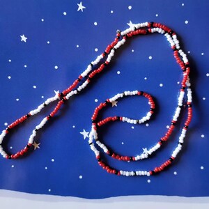 May include: Two beaded necklaces, one longer than the other, with alternating red, white, and black beads. The necklaces are on a blue background with white dots.