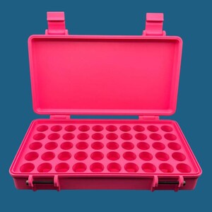 May include: A bright pink rectangular storage case with an open lid, featuring a grid of forty-eight circular indentations for organising small items. The case has two secure latches on the front and two hinges on the back.