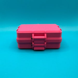 Puede incluir: Un estuche de almacenamiento rectangular de color rosa intenso con un acabado mate texturizado. El estuche cuenta con un mecanismo de cierre con bisagras seguro centrado en el borde frontal, con un dise&ntilde;o robusto y esquinas redondeadas.