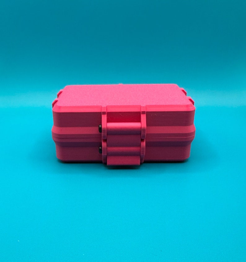 Puede incluir: Un estuche de almacenamiento rectangular de color rosa intenso con un acabado mate texturizado. El estuche cuenta con un mecanismo de cierre con bisagras seguro centrado en el borde frontal, con un dise&ntilde;o robusto y esquinas redondeadas.