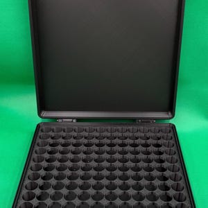 Puede incluir: Un estuche de almacenamiento rectangular negro con tapa abatible y un inserto interior texturizado que presenta una cuadr&iacute;cula de cien compartimentos circulares. El estuche est&aacute; hecho de material negro mate y tiene dos cierres.