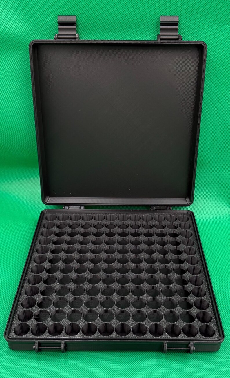 Puede incluir: Un estuche de almacenamiento rectangular negro con tapa abatible y un inserto interior texturizado que presenta una cuadr&iacute;cula de cien compartimentos circulares. El estuche est&aacute; hecho de material negro mate y tiene dos cierres.
