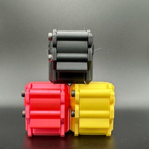 K&ouml;nnte beinhalten: Drei rechteckige, 3D-gedruckte Fidget-Spielzeuge, die in einer Pyramidenform gestapelt sind. Die obere Einheit ist schwarz, w&auml;hrend die beiden unteren Einheiten rot und gelb sind. Jedes Ger&auml;t verf&uuml;gt &uuml;ber eine Reihe paralleler, horizontaler Rollen, die mit kleinen Metallschrauben befestigt sind.