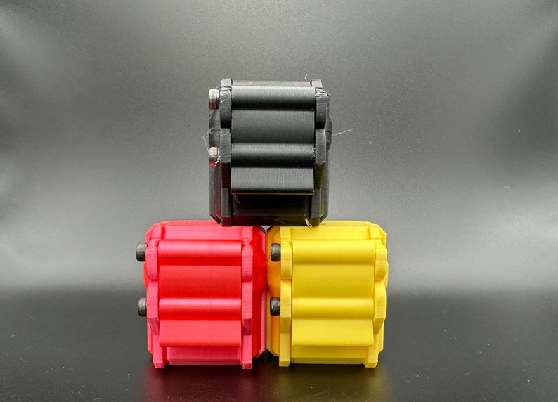 K&ouml;nnte beinhalten: Drei rechteckige, 3D-gedruckte Fidget-Spielzeuge, die in einer Pyramidenform gestapelt sind. Die obere Einheit ist schwarz, w&auml;hrend die beiden unteren Einheiten rot und gelb sind. Jedes Ger&auml;t verf&uuml;gt &uuml;ber eine Reihe paralleler, horizontaler Rollen, die mit kleinen Metallschrauben befestigt sind.