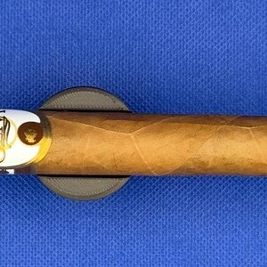 May include: A brown cigar with a white band that says "Oliva" on it. The cigar is resting on a black cigar rest.
