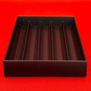 K&ouml;nnte beinhalten: Ein schwarzes Kunststofftablett mit f&uuml;nf gleichm&auml;&szlig;ig verteilten Rillen. Das Tablett ist zum Aufbewahren und Organisieren von Gegenst&auml;nden gedacht.
