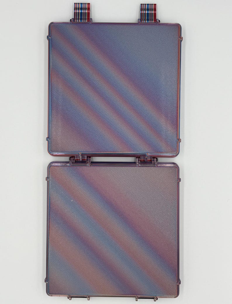 May include: A square, hinged, translucent purple plastic case with a textured surface featuring diagonal iridescent color shifts. The case has two small, plaid-patterned fabric tabs attached to the top edge for opening and closing.