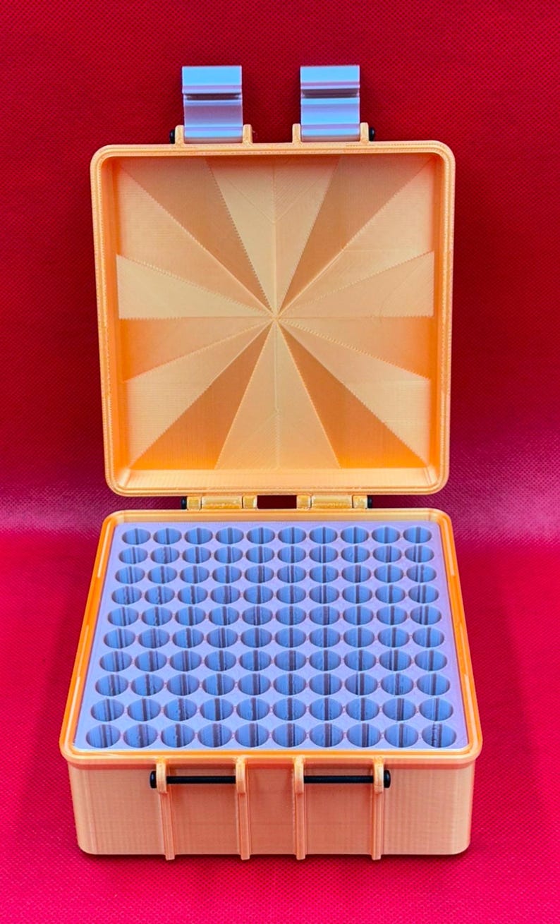 May include: A square orange storage case with a hinged lid featuring a sunburst pattern. The interior contains a light purple insert with a grid of one hundred circular holes for organizing small items. The case has two front latches.