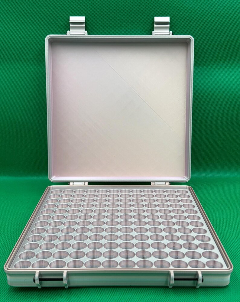 Puede incluir: Un estuche de almacenamiento rectangular de color plateado con tapa abatible, que cuenta con una bandeja interior cuadriculada con numerosos compartimentos circulares para organizar objetos peque&ntilde;os. El estuche tiene dos cierres seguros.