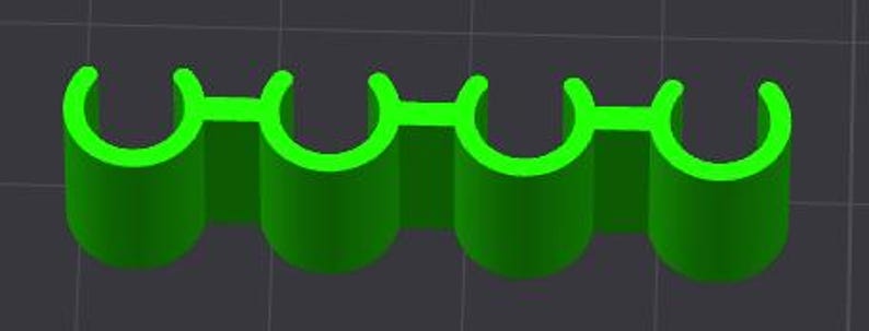 May include: A 3D-rendered, bright green object with four cylindrical sections connected by a flat, horizontal bar. Each cylinder has a curved top, creating a series of four connected arches. The object is set against a dark gray background.