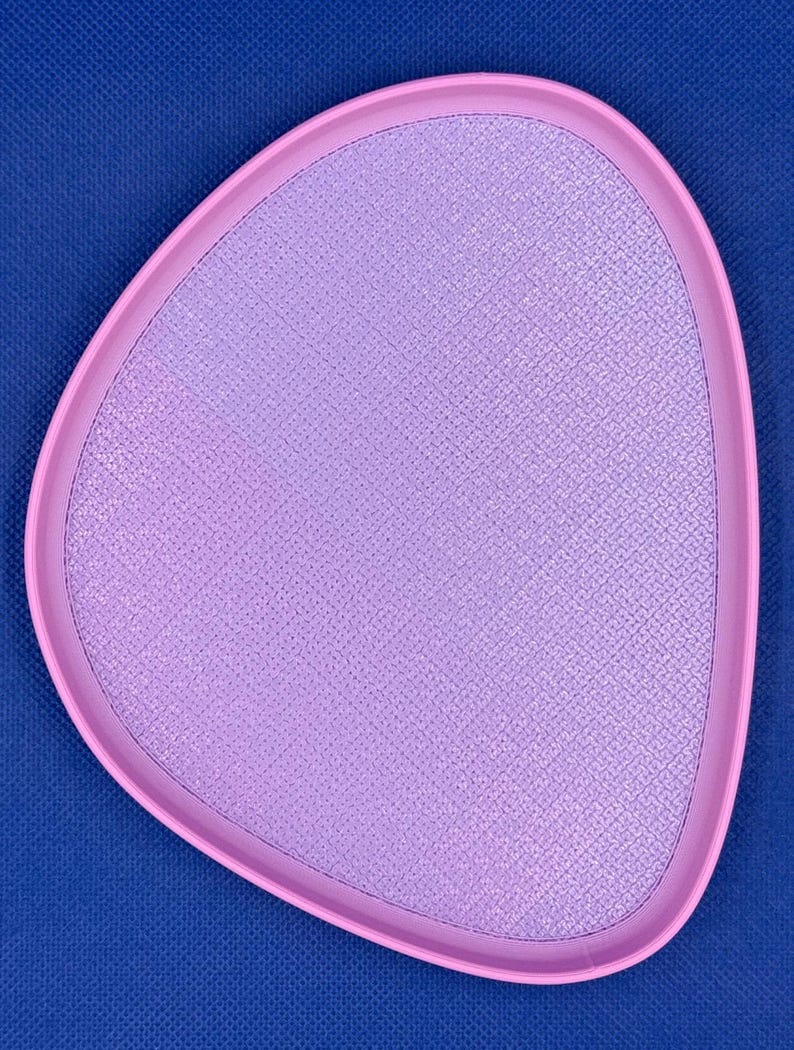 May include: A light pink, oval-shaped tray with a textured surface. The tray has a slightly raised edge.