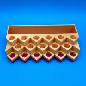 May include: A tiered, 3D-printed organizer featuring a rectangular storage compartment at the back and multiple circular slots arranged in a zigzag pattern. The structure is primarily gold-colored with a vibrant magenta base layer.