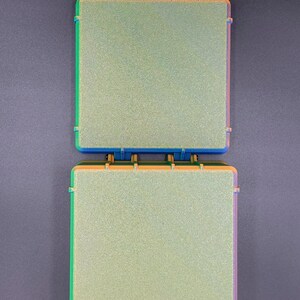 May include: Two square-shaped, light green, textured, plastic boxes with blue, orange, and green trim. The boxes are stacked on top of each other.