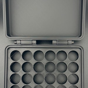 May include: A black, rectangular, 3D-printed storage case with a hinged lid. The interior base features a grid of twenty-five circular cutouts arranged in five rows and five columns, designed for holding small, round items securely in place.