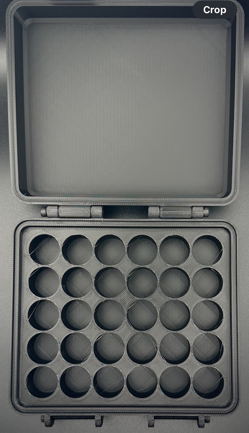 May include: A black, rectangular, 3D-printed storage case with a hinged lid. The interior base features a grid of twenty-five circular cutouts arranged in five rows and five columns, designed for holding small, round items securely in place.