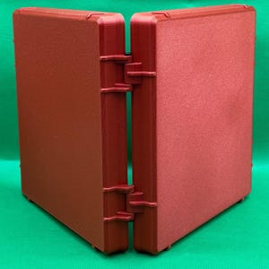 May include: A red, hinged, plastic storage box with a textured surface. The box is closed and the two halves are facing each other.