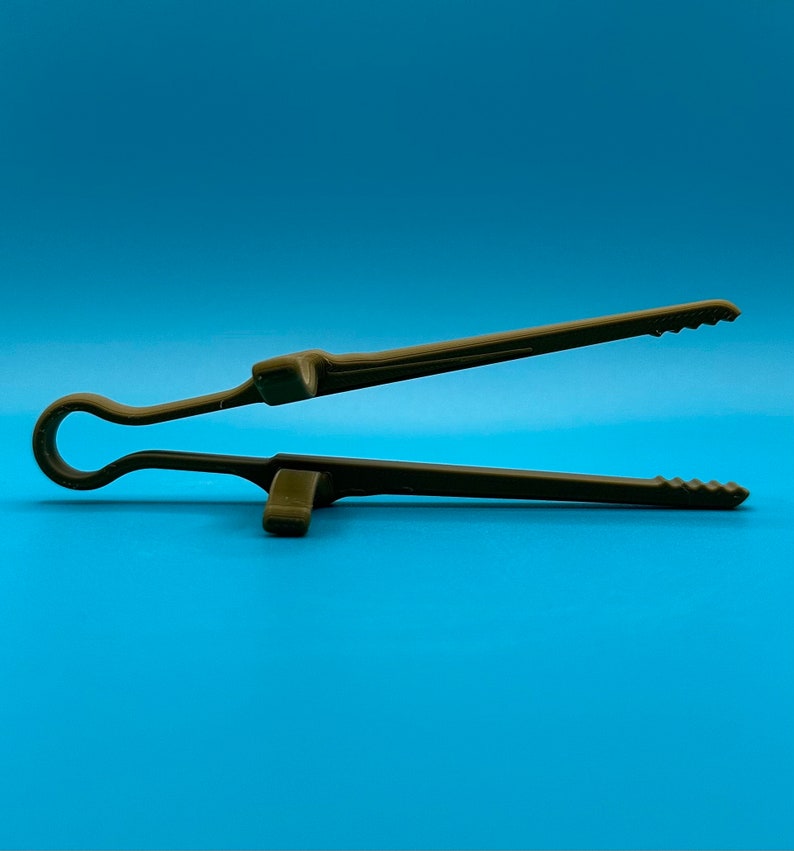 May include: A dark olive green kitchen tong featuring a single-piece molded design with a circular handle loop, two integrated support rests on the exterior of the arms, and serrated gripping edges at the tips for secure handling of food items.
