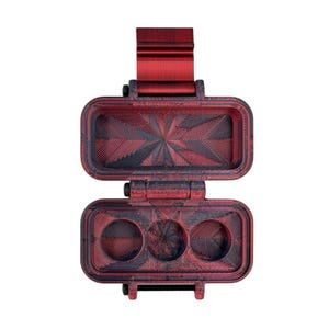 Puede incluir: Un estuche de almacenamiento rectangular con bisagra y acabado jaspeado en rojo y negro. La secci&oacute;n superior es un compartimento abierto, mientras que la inferior presenta tres cavidades circulares. Las superficies interiores muestran un patr&oacute;n geom&eacute;trico de estrella texturizado.