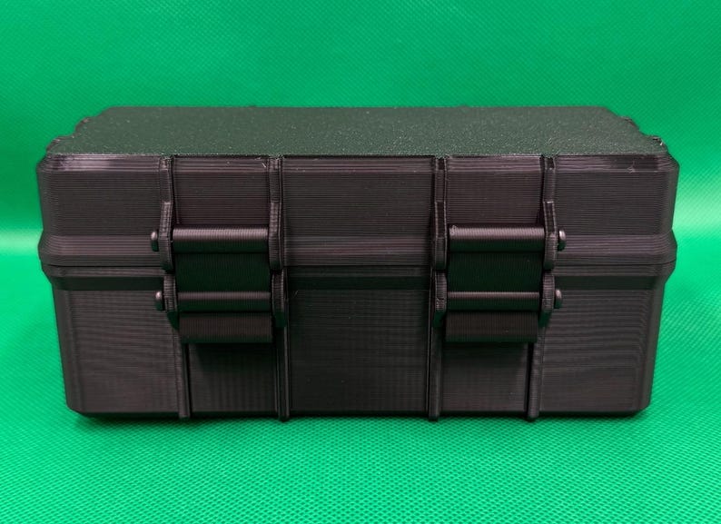 Puede incluir: Una caja de almacenamiento rectangular negra con una superficie texturizada y una tapa plana. La parte frontal del contenedor cuenta con dos mecanismos de cierre verticales que aseguran la tapa a la base, ofreciendo una soluci&oacute;n de almacenamiento robusta.