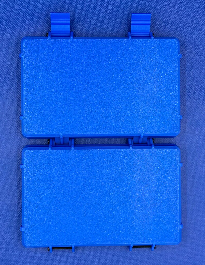 K&ouml;nnte beinhalten: Ein rechteckiger Aufbewahrungskoffer aus blauem Kunststoff mit strukturierter Oberfl&auml;che, bestehend aus zwei klappbaren Abschnitten, die durch ein Mittelgelenk verbunden sind, und zwei blauen Schnappverschl&uuml;ssen.