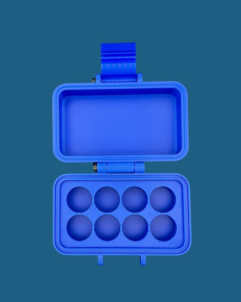 May include: A bright blue rectangular storage case with a hinged lid. The interior features a top compartment with a smooth base and a bottom section containing eight circular recessed slots arranged in two rows of four for organizing small items.