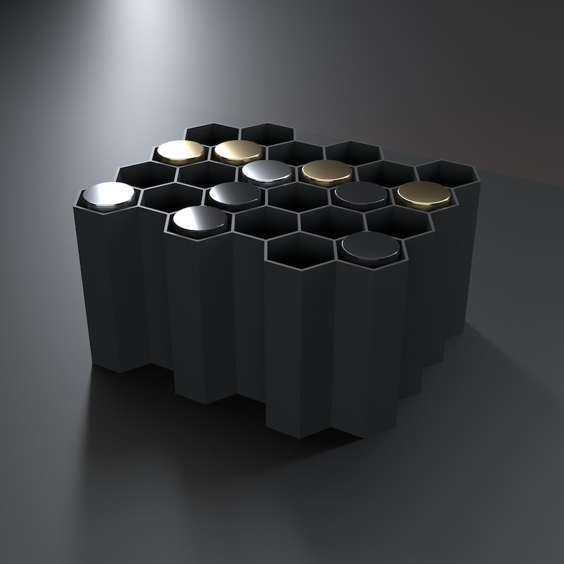 May include: A matte black honeycomb-shaped organizer featuring multiple hexagonal compartments. Several compartments are capped with circular lids in metallic silver, gold, and black finishes, creating a contrast against the dark structure.