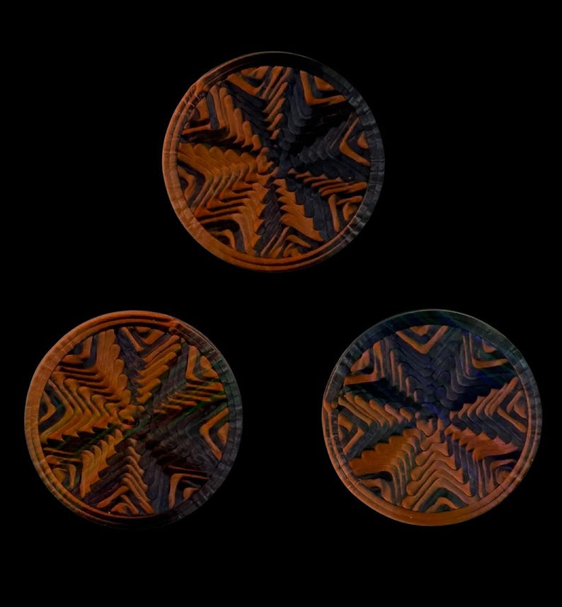 May include: Three circular wooden coasters featuring a complex, layered geometric pattern in alternating shades of deep orange, brown, and dark charcoal gray. Each coaster displays a radial, star-like design with carved, textured grooves.