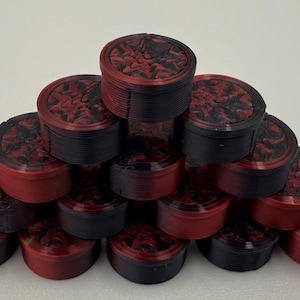 May include: A pyramid arrangement of small, cylindrical containers. Each container features a black and red marbled lid with a textured, swirling pattern. The sides of the containers are solid black or red, showing a layered, ribbed construction.