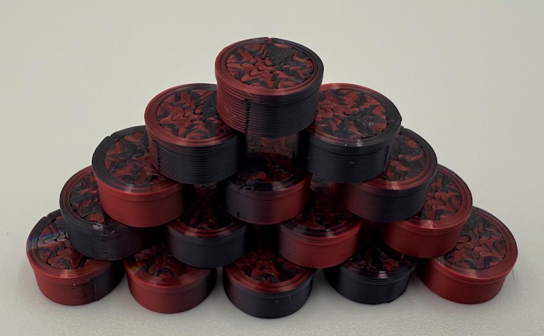 May include: A pyramid arrangement of small, cylindrical containers. Each container features a black and red marbled lid with a textured, swirling pattern. The sides of the containers are solid black or red, showing a layered, ribbed construction.