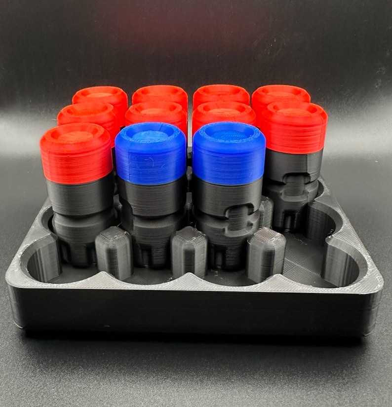 May include: A black 3D-printed storage tray holding twelve cylindrical components. Each component features a black base and a colored top cap, with ten red caps and two blue caps arranged in a grid. The tray has molded slots for each unit.