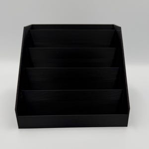 May include: A black, tiered display stand with four shelves. The stand is angled, with each shelf slightly recessed. The stand is made of a solid, matte black material, and is suitable for displaying small items.