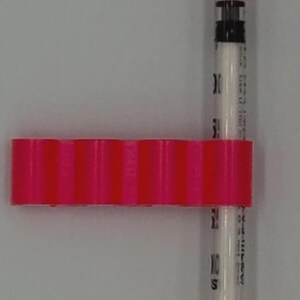 May include: A medical syringe with an orange cap and plunger, connected to a pink, ridged, rectangular component. The syringe is clear with black markings and a white interior. The components are set against a white background.