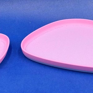 May include: Two pink and blue oval-shaped ceramic trays. The larger tray is in the background and the smaller tray is in the foreground.