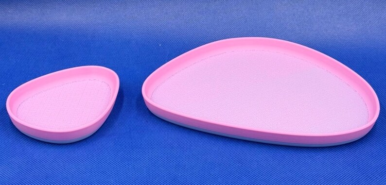 May include: Two pink and blue oval-shaped ceramic trays. The larger tray is in the background and the smaller tray is in the foreground.