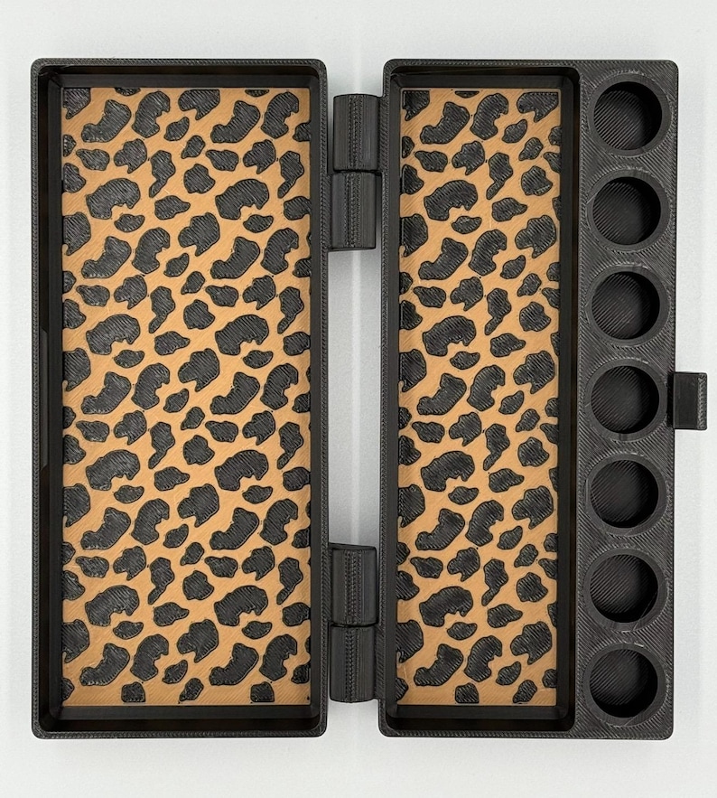 May include: A black rectangular hinged case featuring a tan interior with a black leopard print pattern. The right side of the case includes a column of seven circular cutouts designed for holding small cylindrical items securely.