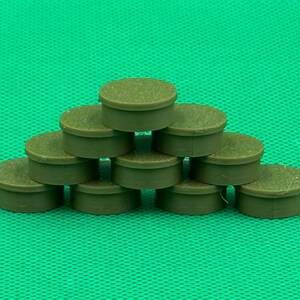 May include: A collection of ten small, round, olive-green plastic caps arranged in a pyramid stack. Each cap features a flat top surface and a short, cylindrical side wall with a smooth, uniform finish, creating a structured, layered display.