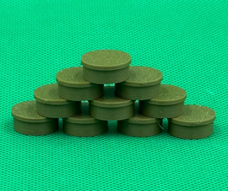 May include: A collection of ten small, round, olive-green plastic caps arranged in a pyramid stack. Each cap features a flat top surface and a short, cylindrical side wall with a smooth, uniform finish, creating a structured, layered display.