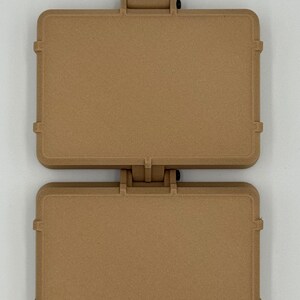 Puede incluir: Una funda con bisagras de color marr&oacute;n claro con forma rectangular. La funda est&aacute; dividida en dos secciones, conectadas por una bisagra en la parte superior. Cada secci&oacute;n tiene una forma rectangular con esquinas redondeadas y una superficie texturizada. La funda tiene un pestillo en la parte inferior.