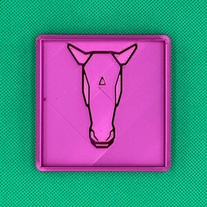 K&ouml;nnte beinhalten: Eine rosa Plastikplakette mit einer schwarzen Umrandung eines Pferdekopfes.